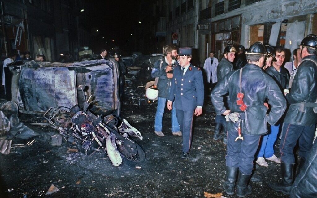 Cette photo d'archives montre des pompiers debout près de l'épave d'une voiture et d'une motocyclette après un attentat à la bombe contre la synagogue de la rue Copernic, causant la mort de quatre personnes prise rue Copernic à Paris, le 3 octobre 1980. (Crédit : AFP/STF)