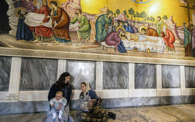 Des pèlerins chrétiens assis près d'une mosaïque représentant le retrait du corps de Jésus-Christ de la croix par la pierre d'onction (non illustrée) lors de la messe catholique du dimanche des Rameaux, à l'église du Saint-Sépulcre, à Jérusalem, le 2 avril 2023. (Crédit : Menahem Kahana/AFP)