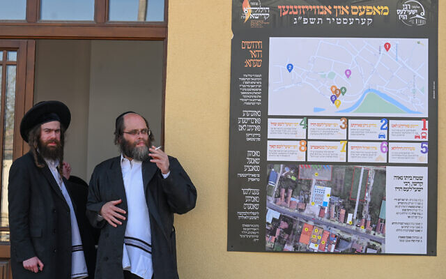 Des Juifs hassidiques attendent le début d'une cérémonie commémorative à côté d'une carte géante de l'événement dans l'ancienne maison de feu le rabbin miracle Yeshaya Steiner, également connu sous le nom de Rebbe Shayale, dans le village de Bodrogkeresztur, en Hongrie, le 23 avril 2023, lors d'un pèlerinage de juifs hassidiques à l'occasion du 98e anniversaire de la mort du rabbin Steiner. (Crédit :ATTILA KISBENEDEK / AFP)