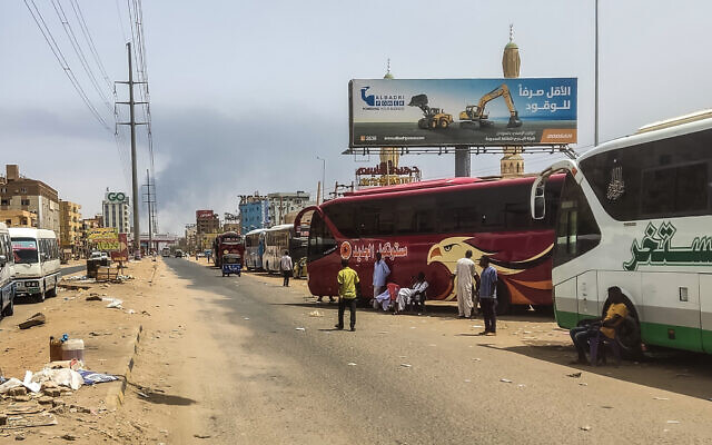 Des personnes attendent à côté de bus de passagers alors que de la fumée se dégage dans une zone de Khartoum où les combats se poursuivent entre l'armée soudanaise et les forces paramilitaires, le 28 avril 2023. (Crédit : AFP)