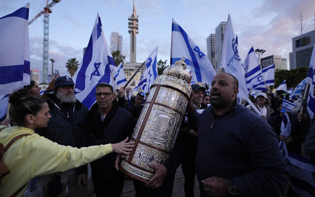 Des Israéliens de droite marchant avec la Torah lors d'un rassemblement de soutien aux plans du gouvernement du Premier ministre Benjamin Netanyahu visant à réformer le système judiciaire, à Tel Aviv, le 30 mars 2023. (Crédit : Ariel Schalit/AP)