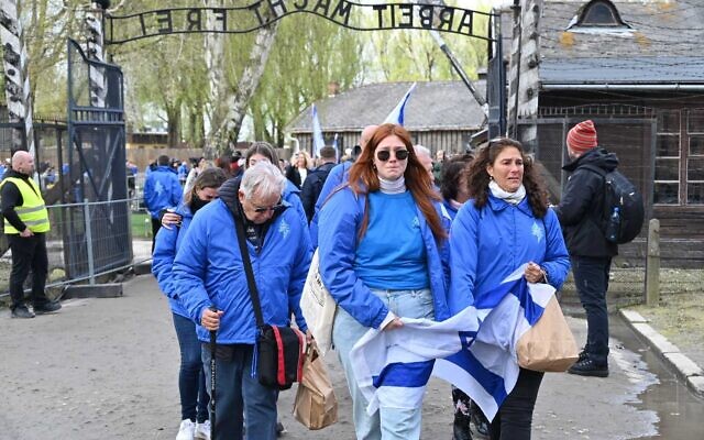À Auschwitz, des survivants de la Shoah et leurs compagnons franchissant la porte "Arbeit Macht Frei" lors de la Marche des vivants, le 18 avril 2023. (Crédit : Canaan Lidor/Times of Israel)