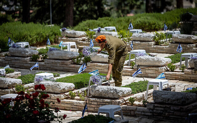 Un soldat israélien dépose des fleurs et des bougies sur les tombes des soldats tombés au champ d’honneur, au cimetière militaire du mont Herzl à Jérusalem, le 3 mai 2022, en vue de Yom HaZikaron. (Crédit : Yonatan Sindel/Flash90)