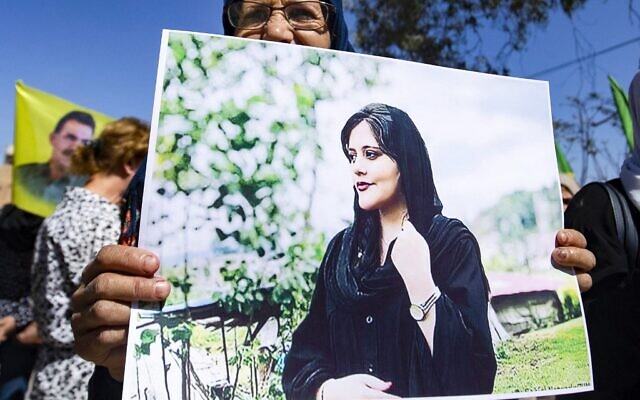 Une femme brandissant une pancarte représentant une photo de Mahsa Amini, 22 ans, une Iranienne décédée alors qu'elle était détenue par les autorités iraniennes, lors d'une manifestation dans la ville de Hasakeh, dans le nord-est de la Syrie, le 25 septembre 2022. (Crédit : Delil Souleiman/AFP)