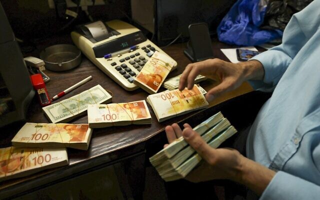 Un Palestinien compte des piles de billets de banque à un comptoir de change dans la ville de Ramallah, en Cisjordanie, le 5 octobre 2021. (Crédit :ABBAS MOMANI / AFP)