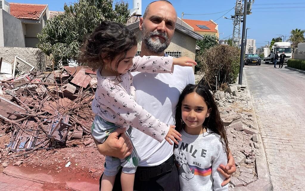 Nissim Azoulai et ses deux filles devant les décombres d'un tir direct de roquette dans leur quartier d'Ashkelon, le 11 mai 2023 (Crédit : Carrie Keller-Lynn/The Times of Israel)