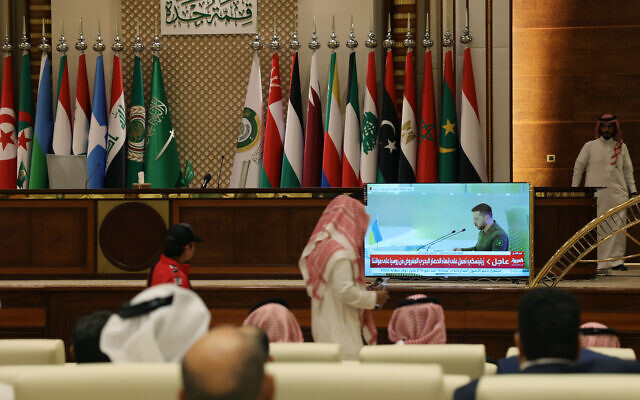 Les délégués des médias regardent sur un écran le président ukrainien Volodymyr Zelensky s'adresser au sommet de la Ligue arabe à Djeddah le 19 mai 2023. (Crédit : Fayez Nureldine / AFP)