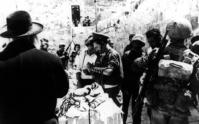 Un homme distribue des châles de prière et des phylactères aux soldats israéliens qui prient au mur Occidental, dans la Vieille Ville de Jérusalem, au lendemain de sa capture aux Jordaniens pendant la guerre des Six jours, le 8 juin 1967. (Crédit : AP Photo, File)
