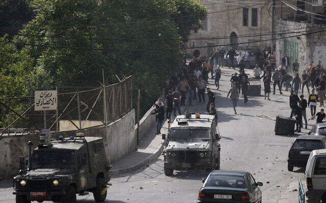 Illustration : Des Palestiniens poursuivent des véhicules militaires israéliens quittant Naplouse, le 9 mai 2023. (Crédit : AP/Majdi Mohammed)