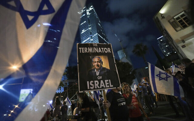 Des manifestants marchant avec des drapeaux israéliens et tenant une banderole représentant le Premier ministre Benjamin Netanyahu lors d'une manifestation contre les projets de son gouvernement de réformer le système judiciaire, à Tel Aviv, le 20 mai 2023. (Crédit : AP Photo/Tsafrir Abayov)