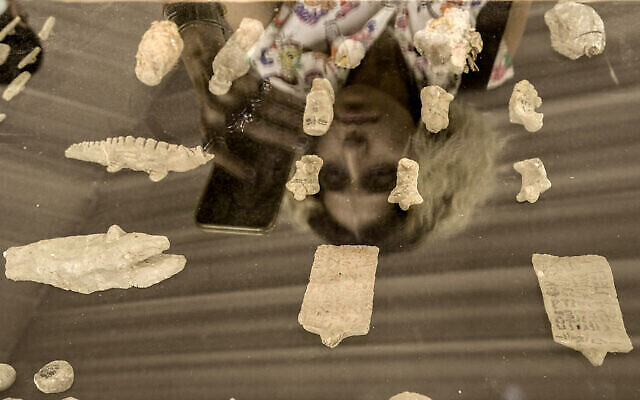 Une visiteuse se reflète sur un panneau sur lequel sont placés des objets anciens récemment mis au jour, alors qu'elle filme le site de la pyramide à degrés de Djéser, à Saqqara, en Égypte, le 27 mai 2023. (Crédit : AP Photo/Amr Nabil)