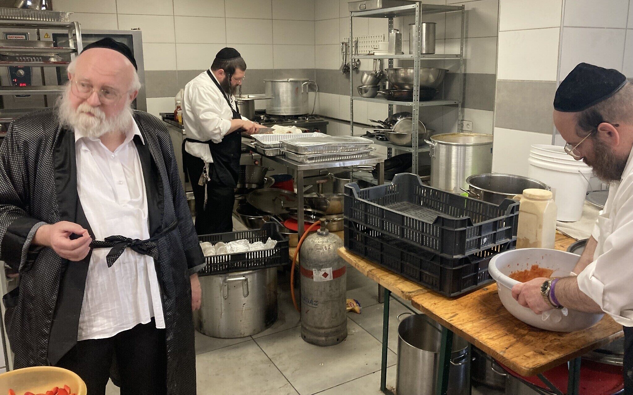 Des cuisiniers et un superviseur de la cacherout préparent la nourriture pour les nombreux invités affamés qui visitent la maison d'hôtes des Friedlanders lors du pèlerinage annuel sur la tombe de Yeshaya Steiner à Bodrogkeresztur, en Hongrie, le 24 avril 2023. (Crédit : Yaakov Schwartz/ Times of Israel)
