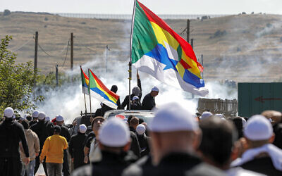 Des vapeurs de gaz lacrymogène emplissant l'air alors que des membres de la communauté druze se rassemblent avec leurs drapeaux pour protester contre un projet israélien d'éoliennes près du village de Majdal Shams sur le plateau du Golan, le 21 juin 2023. (Crédit : Jalaa Marey/AFP)