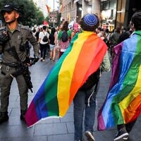 Un garde de la police des frontières israélienne montant la garde alors que des personnes drapées de drapeaux arc-en-ciel défilant lors de la 21e édition du défilé annuel de la Gay Pride de Jérusalem, le 1er juin 2023. (Crédit : Menahem Kahana/AFP)