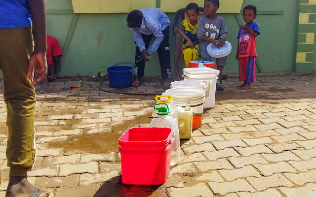 Cette photo prise le 20 juin 2023 montre des hommes et des enfants soudanais déplacés remplissant des conteneurs d'eau à Wad Madani, la capitale de l'État soudanais d'al-Jazirah. (Crédit : AFP)