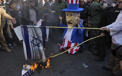 Des manifestants brûlant des représentations des drapeaux américain et israélien tandis qu'un personnage de l'Oncle Sam "réagit" lors d'une manifestation annuelle devant l'ancienne ambassade des États-Unis à Téhéran, en Iran, le 4 novembre 2022. (Crédit : AP Photo/Vahid Salemi)