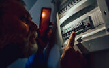 Un homme vérifiant une boîte à fusibles lors d'une panne de courant. (Crédit : Jovanmandic/iStock at Getty Images)