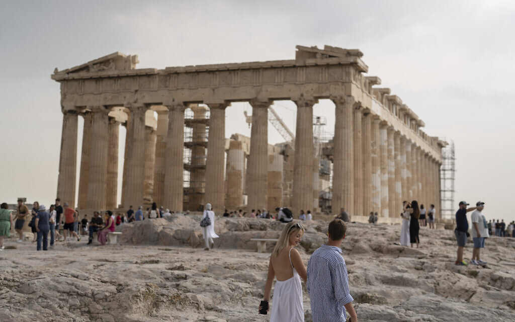 Un couple se promène devant le temple du Parthénon, datant du Ve siècle avant J.-C., sur la colline de l'Acropole d'Athènes, le 31 mai 2023. (Crédit : Petros Giannakouris/AP)