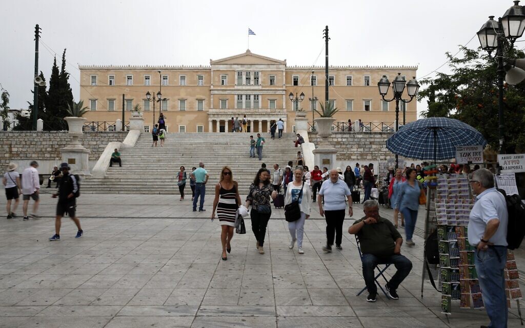 Un vendeur de billets de loterie est assis à son kiosque pendant que les piétons marchent sur la place Syntagma à Athènes, le 27 mai 2019. (Crédit : Thanassis Stavrakis/AP)