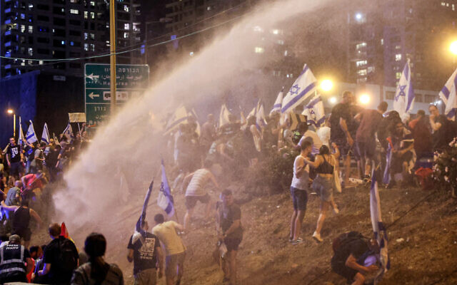 Des manifestants face au canon à eau utilisé par la police anti-émeute pendant un rassemblement contre le plan de refonte du système judiciaire israélien à Tel Aviv, le 18 juillet 2023. (Crédit : JACK GUEZ / AFP)