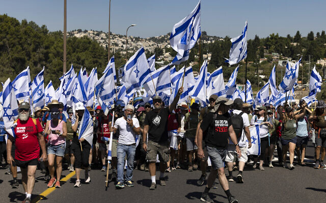 Des manifestants brandissant des drapeaux nationaux israéliens alors qu'ils marchent sur l'autoroute près de la ville de Mevasseret Zion, lors d'une marche de plusieurs jours de Tel Aviv à Jérusalem pour protester contre le projet de loi de révision judiciaire du gouvernement avant un vote au Parlement, le 22 juillet 2023. (Crédit : Menahem Kahana/AFP)