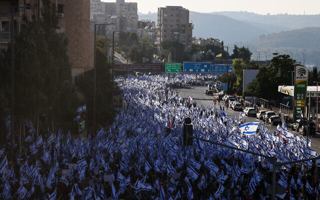  Des dizaines de milliers de manifestants brandissant des drapeaux israéliens alors qu'ils marchent vers Jérusalem, lors d'une marche de plusieurs jours qui a débuté à Tel Aviv pour protester contre la loi de réforme judiciaire du gouvernement avant le vote de la première loi de ce type à la Knesset, le 22 juillet 2023. (Crédit :  Menahem Kahana/AFP)