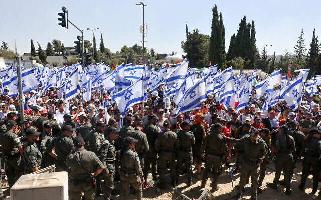 Les forces de police montant la garde alors que les manifestants agitent des drapeaux à l'entrée de la Knesset, à Jérusalem, le 24 juillet 2023. (Crédit : Menahem Kahana/AFP)