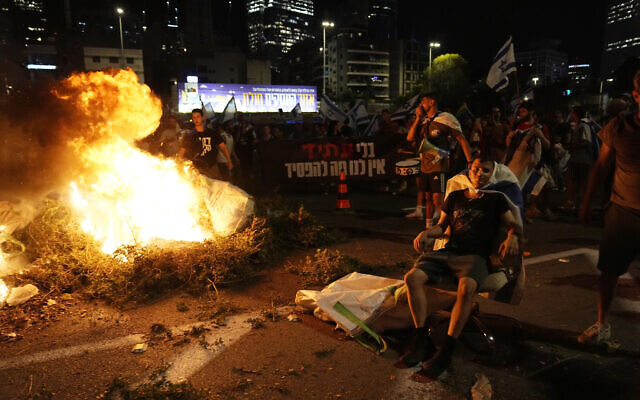 Un feu brûle alors que des Israéliens bloquent l'autoroute Ayalon pour protester contre les plans du gouvernement du Premier ministre Benjamin Netanyahu visant à remanier le système judiciaire, à Tel Aviv, jeudi 20 juillet 2023. (Crédit : Ohad Zwigenberg/AP)