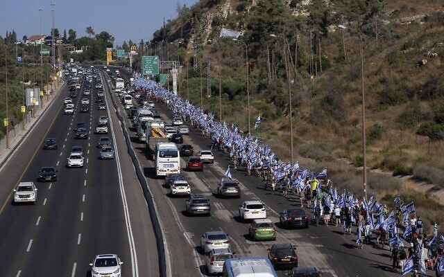  Des Israéliens marchant sur la Route 1 en direction de Jérusalem près du moshav Shoresh, dans le cadre des manifestations contre les projets du gouvernement du Premier ministre Benjamin Netanyahu de remanier le système judiciaire, le 21 juillet 2023. (Crédit :  AP Photo/Ohad Zwigenberg)