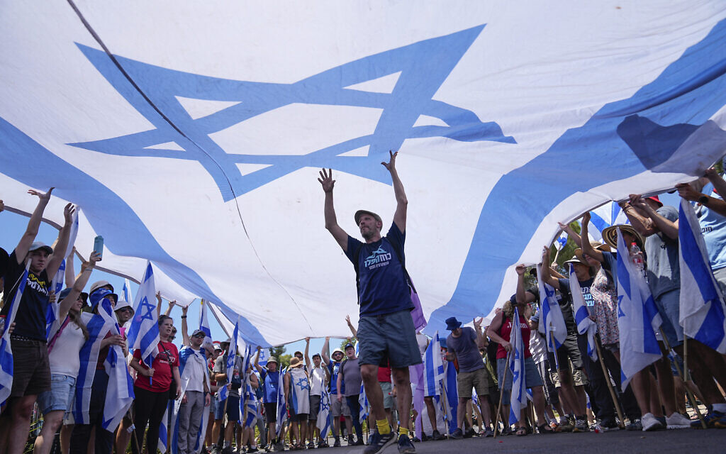 Des manifestants brandissant un grand drapeau israélien lors d'une manifestation contre le gouvernement devant la Knesset, à Jérusalem, le 24 juillet 2023. (Crédit : AP Photo/Ohad Zwigenberg).
