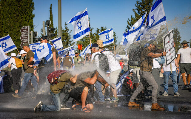 Des manifestants anti-rénovation sont aspergés par un canon à eau de la police alors qu'ils bloquent une route près de la Knesset, le 24 juillet 2023. (Crédit : Chaim Goldberg/Flash90)