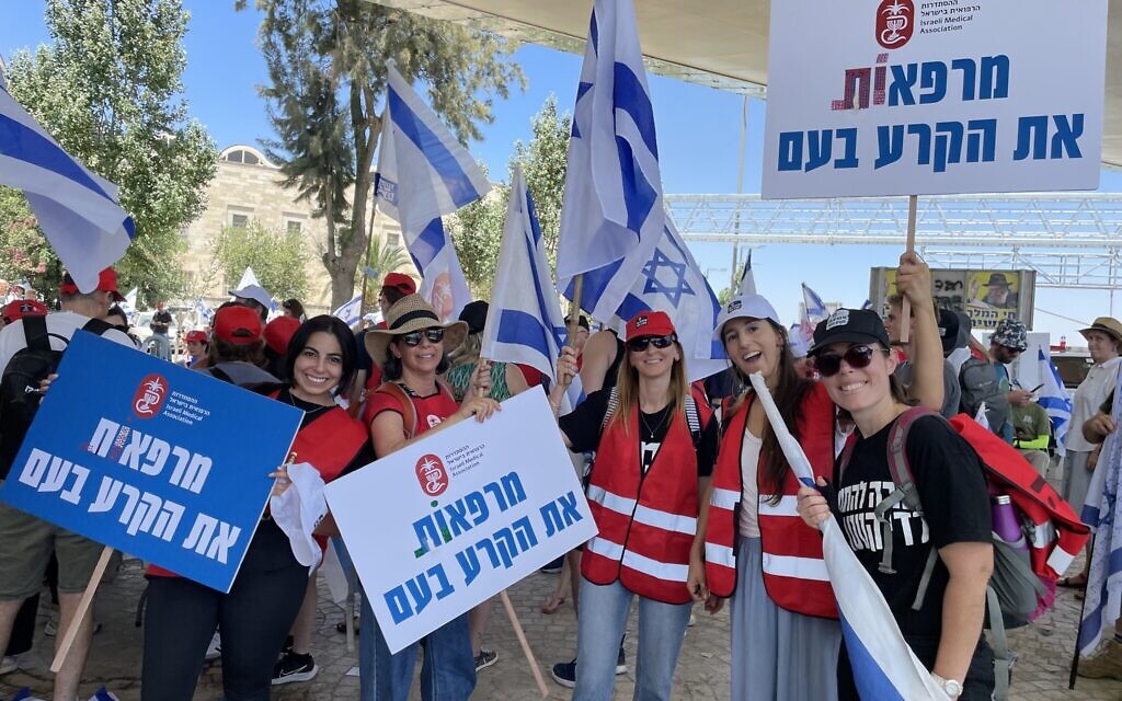 Des médecins tenant des drapeaux israéliens et des pancartes de l'Association médicale israélienne déclarant "Nous guérissons les failles de la nation" lors d'une manifestation contre la refonte judiciaire organisée par l'IMA, à Jérusalem, le 23 juillet 2023. (Crédit : Renée Ghert-Zand/Times of Israel)