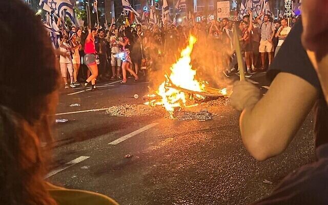 Des manifestants rassemblés autour d'un feu lors d'une manifestation contre la réforme judiciaire du gouvernement, à Tel Aviv, le 24 juillet 2023. (Crédit : Naomi Lanzkron)