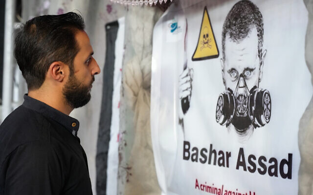 Un homme regardant une affiche représentant le dicateur syrien Bashar el-Assad avec un masque à gaz lors d'un événement marquant le 10e anniversaire des attaques chimiques qui ont tué plus de 1 400 personnes dans la Ghouta, près de la capitale, dans la ville d'Afrin, le 20 août 2023. (Crédit : Rami al-Sayed/AFP)