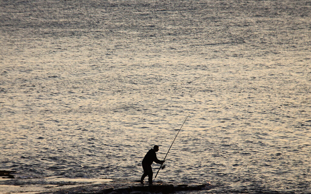 Un pêcheur sur un récif rocheux dans la mer Méditerranée, au nord d'Israël, le 21 décembre 2015. (Crédit : Ariel Schalit/AP Photo)
