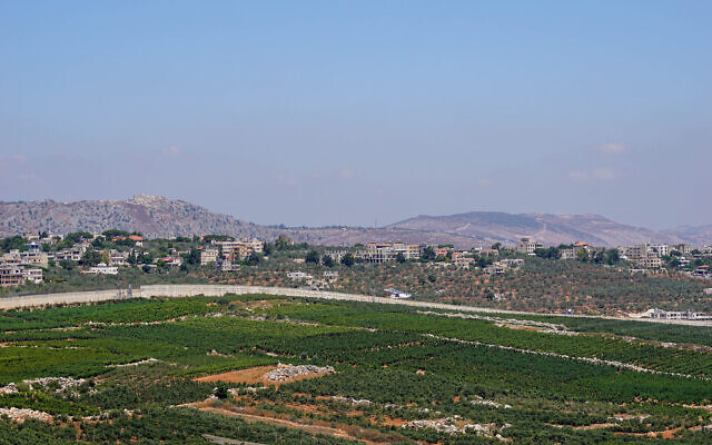 La barrière de sécurité militaire israélienne à la frontière avec le Liban, près de la ville de Metoula, avec la ville libanaise de Kfarkela en arrière-plan, le 2 août 2023. (Crédit : Emanuel Fabian/Times of Israel)