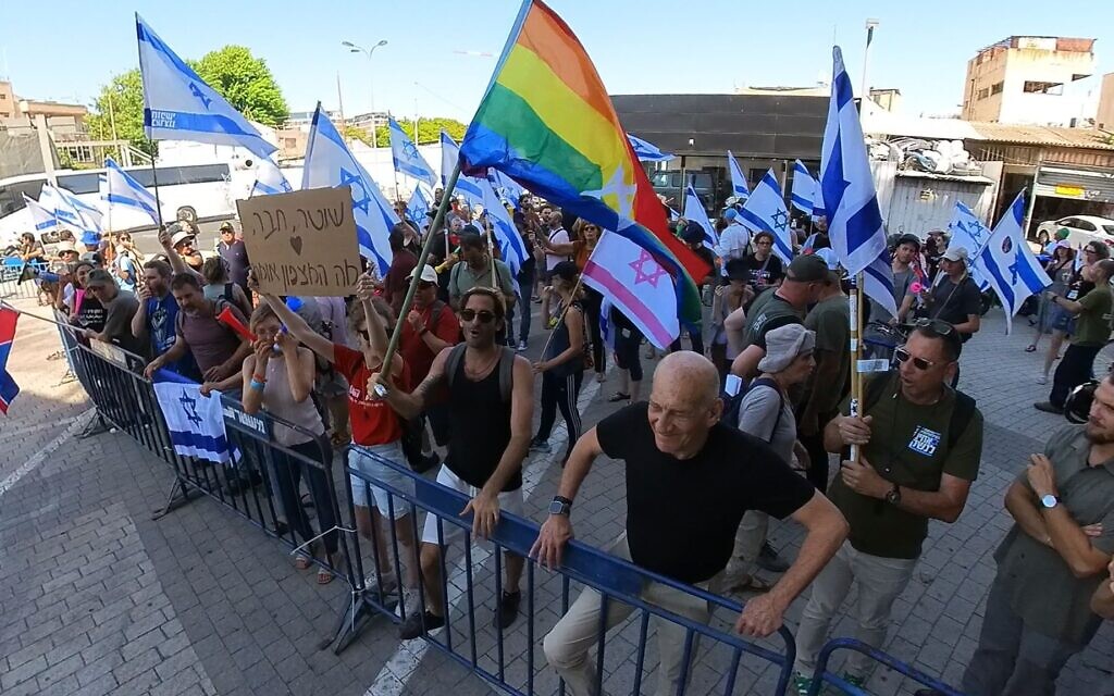 L'ancien premier ministre Ehud Olmert (en bas à droite) et une femme tenant une pancarte "Policier, ami, que dit la conscience ?" devant le poste de police de Shalma, à Tel Aviv, le 1er août 2023. (Crédit : @sha_b_p)