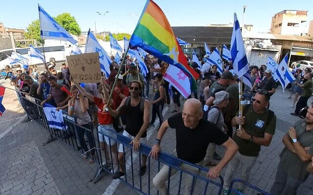 L'ancien premier ministre Ehud Olmert (en bas à droite) et une femme tenant une pancarte "Policier, ami, que dit la conscience ?" devant le poste de police de Shalma, à Tel Aviv, le 1er août 2023. (Crédit : @sha_b_p)
