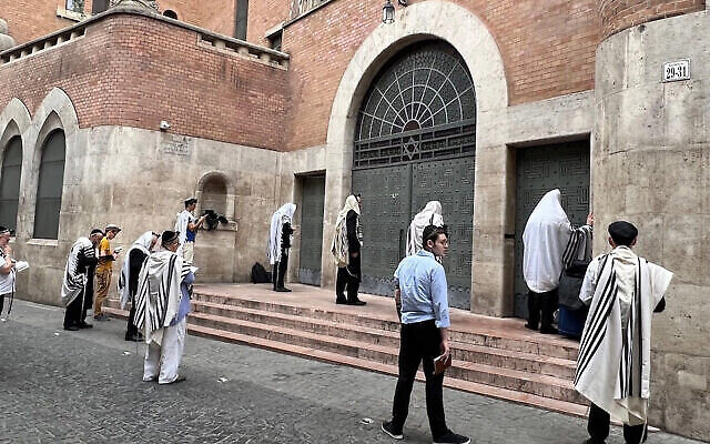 Des fidèles lors de la prière du matin devant les portes verrouillées de la synagogue de la rue Kazinczy à Budapest, en Hongrie, le 21 juillet 2023. (Crédit : David Kelsey/JTA)