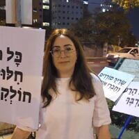 Fay Sukenik manifeste contre l'aide que le ministre Meir Porush aurait apportée à un délinquant sexuel. Sur sa pancarte, on peut lire : "Lorsque le nom de Dieu est profané par un rabbin, il n'est pas digne de respect' près du domicile de ce dernier, le 31 août 2023 à Jérusalem, en Israël. (Crédit : Autorisation/Sukenik)