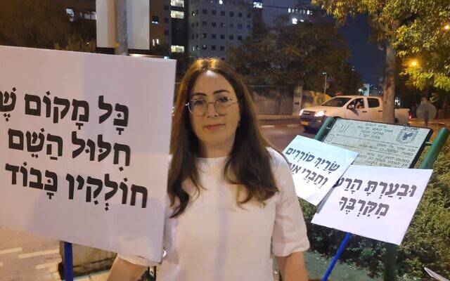 Fay Sukenik manifeste contre l'aide que le ministre Meir Porush aurait apportée à un délinquant sexuel. Sur sa pancarte, on peut lire : "Lorsque le nom de Dieu est profané par un rabbin, il n'est pas digne de respect' près du domicile de ce dernier, le 31 août 2023 à Jérusalem, en Israël. (Crédit : Autorisation/Sukenik)