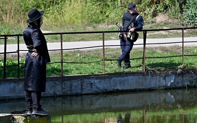 Un juif hassidique et un policier ukrainien armé sont vus au bord d’un lac à Ouman, dans le centre de l’Ukraine, le 26 septembre 2022. (Crédit : Sergei Supinsky/AFP)