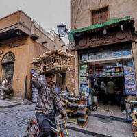 Un livreur portant une charge de pain sur sa tête alors qu'il circule à vélo dans une rue des vieux quartiers du Caire, le 27 février 2023. (Crédit : Khaled Desouki/AFP)