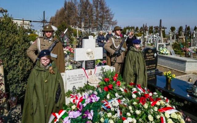 Des soldats montent la garde pendant que les gens déposent des couronnes de fleurs lors d'une cérémonie sur la tombe de la famille Ulma, une famille polonaise qui s'est sacrifiée alors qu'elle cachait des Juifs pendant la Shoah, à Markowa, en Pologne, le 17 mars 2016. (Crédit : Wojtek Radwanski /AFP)
