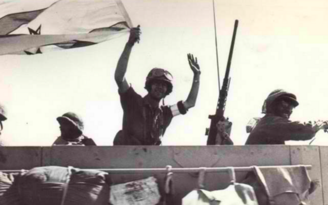 Un soldat de l’armée israélienne brandissant un drapeau israélien sur le chemin de Damas, pendant la Guerre du Kippour, en octobre 1973. (Crédit : Archives de l'État)
