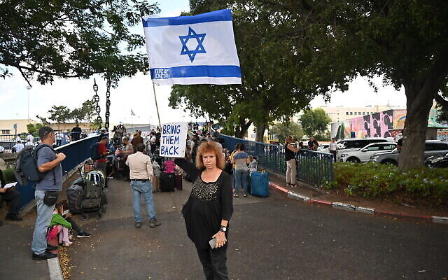 Heda Amir tient une pancarte sur laquelle on peut lire "Bring them back" et un drapeau israélien près de passagers qui attendent de monter à bord d'un navire d'évacuation organisé par l'ambassade des États-Unis à Haïfa, le 16 octobre 2023. (Crédit : Canaan Lidor/Times of Israel)