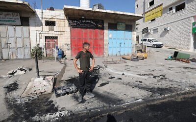 Un Palestinien inspectant les dégâts, après une attaque nocturne par des résidents d'implantations israéliens, dans le village de Huwara en Cisjordanie, le 6 octobre 2023. (Crédit : Jaafar Ashtiyeh/AFP)