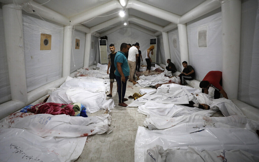 Des personnes se tenant au-dessus des corps des Palestiniens tués lors d'une attaque sur l'hôpital Ahli Arab dans le centre de Gaza après qu'ils aient été transportés à l'hôpital al-Shifa, le 17 octobre 2023. (Crédit : Dawood Nemer/AFP)