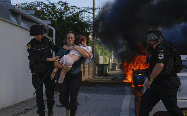 Des policiers évacuant une femme et un enfant d'un site touché par une roquette tirée depuis la bande de Gaza, à Ashkelon, dans le sud d'Israël, le 7 octobre 2023. (Crédit : Tsafrir Abayov/AP Photo)