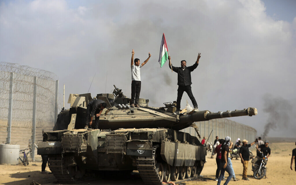 Des Palestiniens brandissant leur drapeau et célébrant près d'un char israélien détruit à la barrière de sécurité, à la frontière de la Bande de Gaza à l'est de Khan Younis, le 7 octobre 2023. (Crédit : Yousef Masoud/AP Photo)